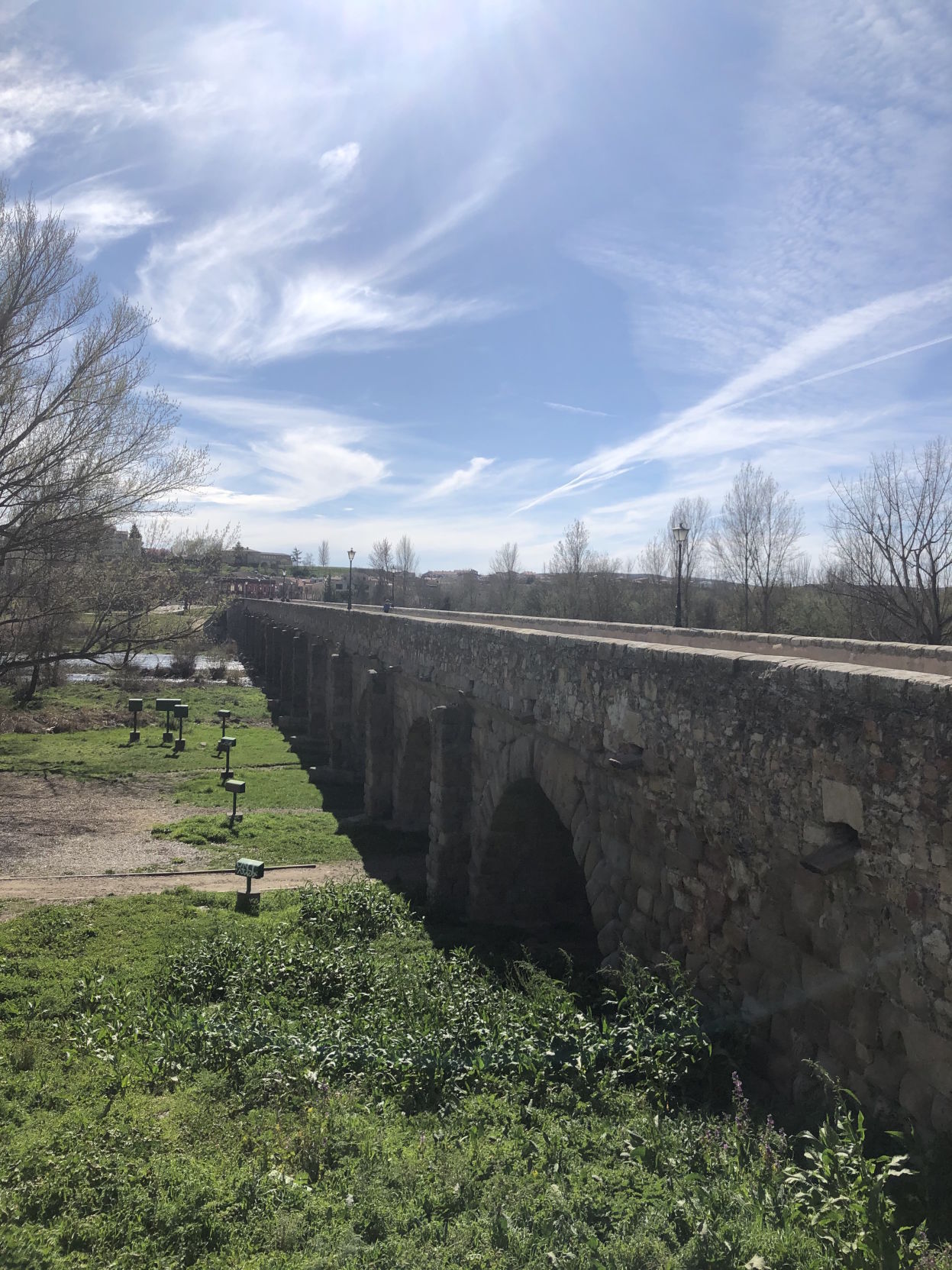 The Puente Romano (Roman Bridge) is surrounded by grass and trees as street lamps line the edges of the bridge